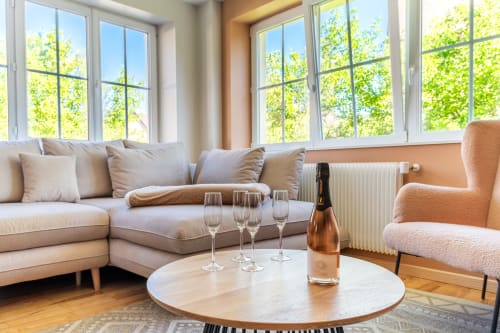 Luminoso salón de lujo en Les Ambrades con sofá beige, sillón, mesa redonda, botella de champagne y copas