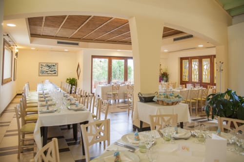 Elegante sala da pranzo dell'Hotel Ristorante alle Querce a Castelbuono con lunghi tavoli, sedie in legno e luce naturale da