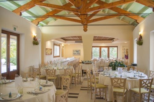 Elegante sala da pranzo dell'Hotel Ristorante alle Querce a Castelbuono con travi in legno, tavoli rotondi e grandi finestre