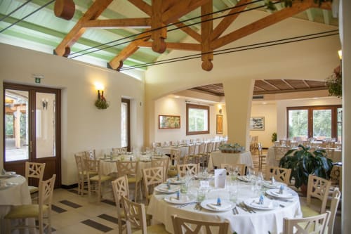Elegante sala da pranzo dell'Hotel Ristorante alle Querce a Castelbuono con travi in legno e tavoli rotondi allestiti.