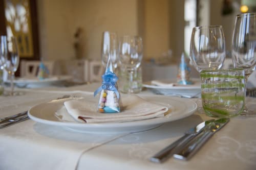 Elegante mise en place all'Hotel Ristorante alle Querce di Castelbuono con piatti bianchi, bomboniera blu e bicchieri.