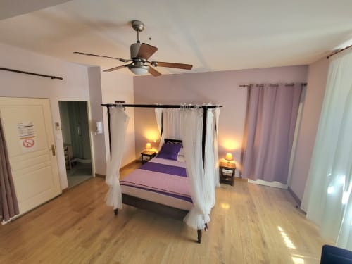 Chambre Violette au Cadran Solaire à Courcelles : lit à baldaquin, parure violette, ventilateur et lumière chaleureuse