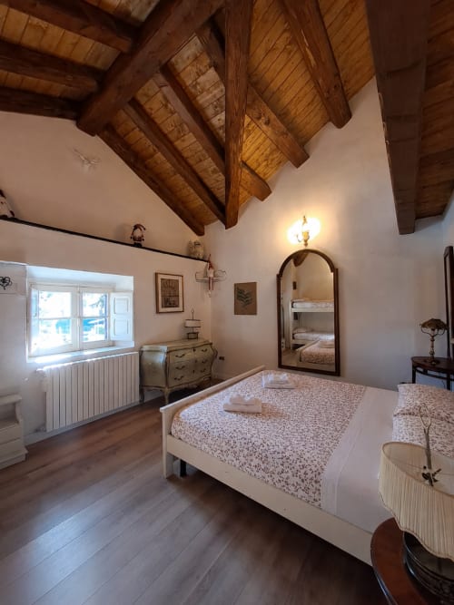 Ampia camera da letto nella villa Antico Chalet Momosa, Ovindoli, con travi di legno a vista, letto bianco, specchio, viste montane