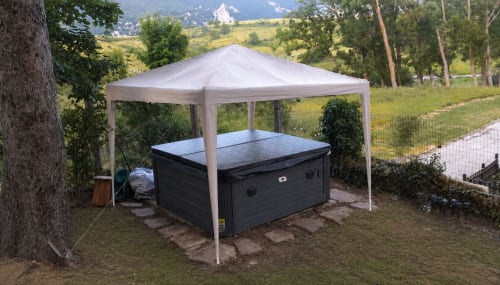 Vasca idromassaggio nera sotto gazebo bianco nel giardino del resort montano di Ovindoli con vette alpine sullo sfondo