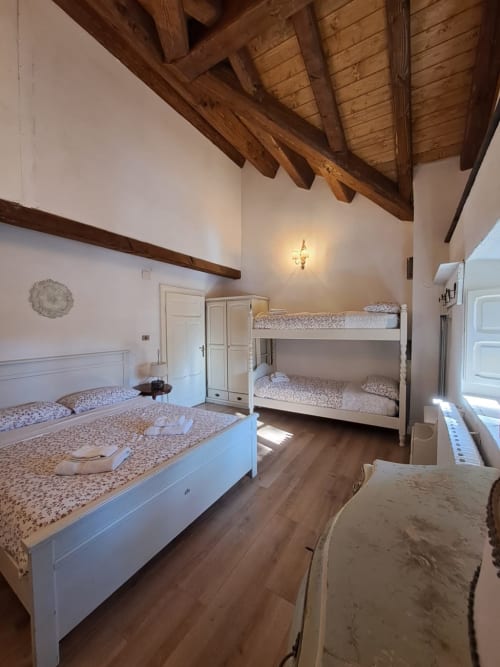 Ampia camera da letto in villa Antico Chalet Momosa con travi in legno a vista, letto matrimoniale bianco, letti a castello e pavimento in legno