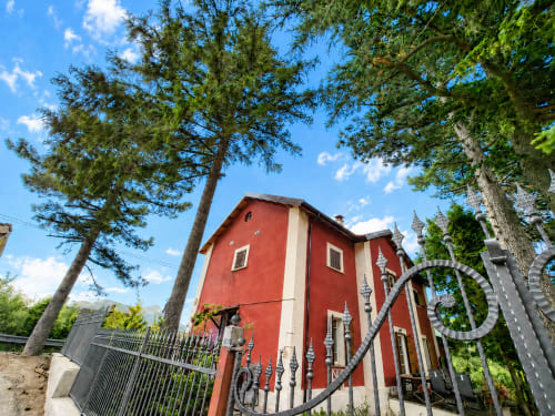 Villa chalet rosso a Ovindoli circondato da pini e montagne con cancello in ferro battuto
