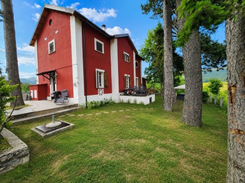 Chalet Maxi Momosa, villa rosso e bianca a Ovindoli con vista sulle montagne, circondata da alberi alti e prato verde