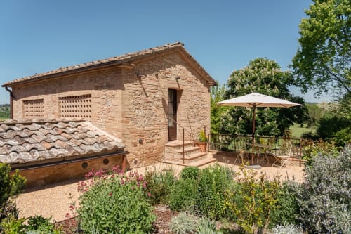 Rustic brick farmhouse at Agriturismo La Frattina in Siena with terracotta roof, garden patio and umbrella.