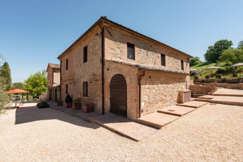 Rustic brick farmhouse at Agriturismo La Frattina in Buonconvento, Siena, with terracotta courtyard and umbrellas