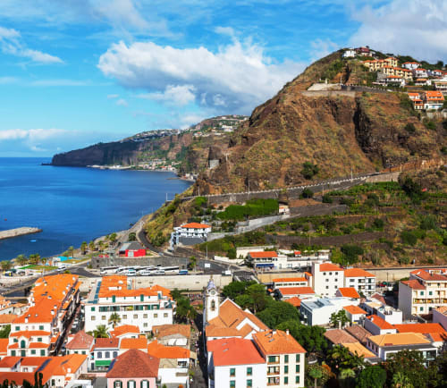 Paisagem urbana de Funchal com edifícios de telhados laranja, oceano azul e escarpas dramáticas na Madeira, Portugal