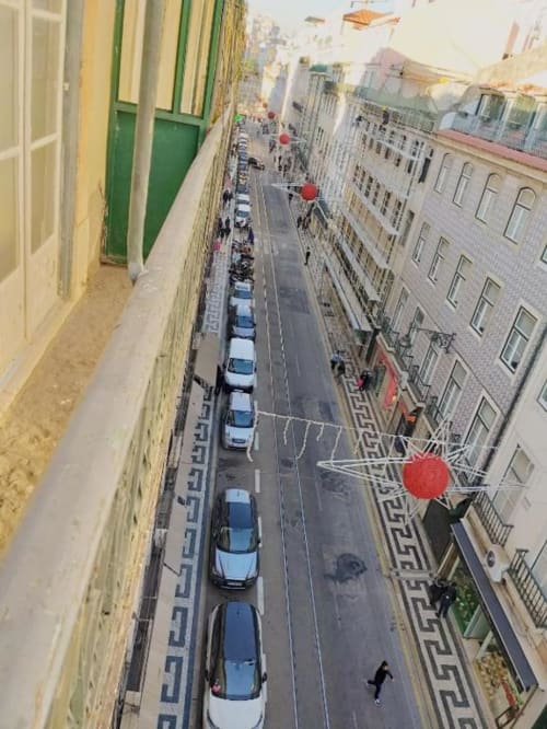 Aerial view of narrow Lisbon street with parked cars, red balloons, and colorful buildings from city apartment
