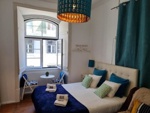 Cozy bedroom in Lisbon apartment with city view, blue velvet bed, turquoise accents, and window seating area