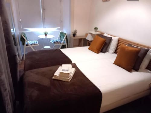Modern bedroom in Lisbon apartment with two beds, brown and white bedding, orange cushions, seating area with chairs by