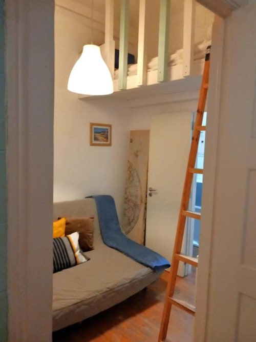 Cozy bedroom in Lisbon apartment with bed, blue mattress, wooden ladder, pendant lamp, and hardwood floors.