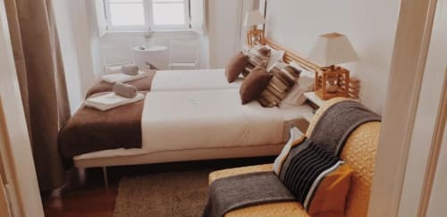 Bright bedroom in Lisbon BnB with two beds, wooden furniture, city view window, and warm brown and cream decor