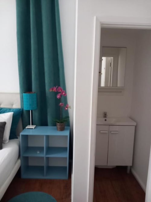 Modern bedroom in Lisbon apartment with teal curtains, blue nightstand, pink orchids, and hardwood floors