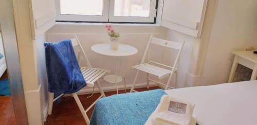 Cozy bedroom seating area in Lisbon apartment with blue towel, round table, white chairs, and city view from window