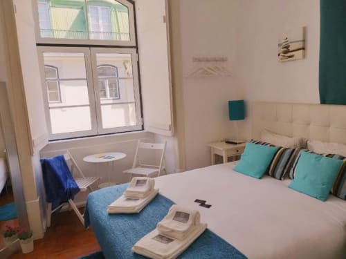 Lisbon apartment bedroom with double bed, turquoise accents, city view window, and work seating area