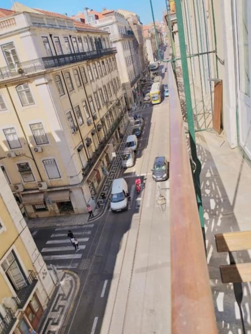 Aerial view of narrow Lisbon street with parked cars and historic pastel-colored buildings from city apartment