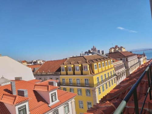 Lisbon rooftop city view with colorful yellow buildings, orange terracotta tiles, and skyline beyond