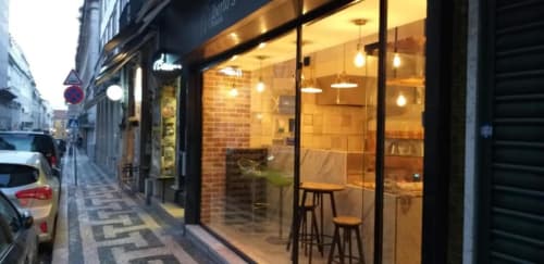 Modern restaurant storefront in Lisbon with warm lighting, exposed brick, and bar seating visible through large windows at