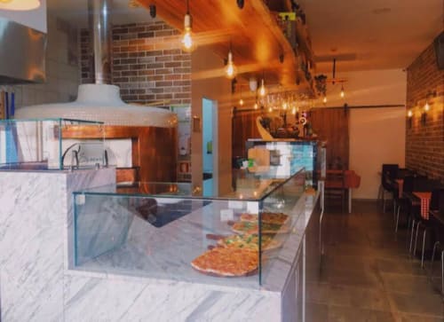 Modern Lisbon apartment kitchen with marble counters, pizza display, exposed brick, pendant lights, and dining area at Charm