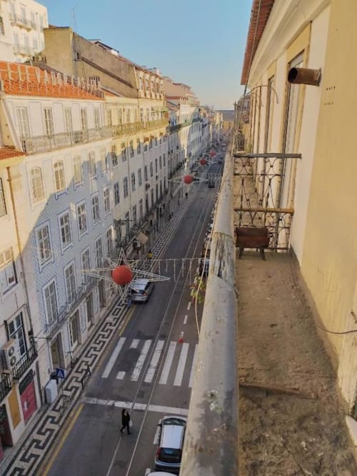 Balcony view of Lisbon street with white buildings, red decorations, and cobblestone square from Charm Discovery Experiences