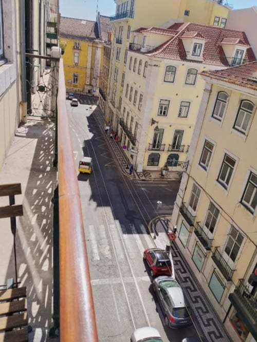 Aerial view of a narrow Lisbon street with colorful buildings, parked cars, and a red tram track below a balcony railing