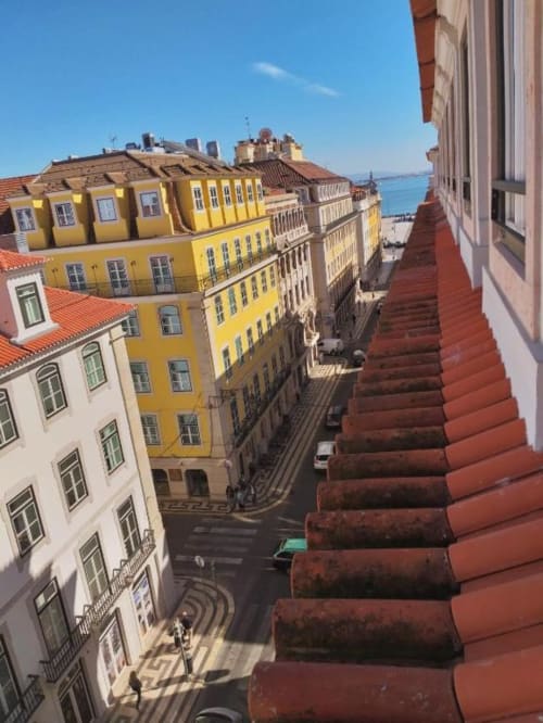 Lisbon city street view from apartment balcony with yellow buildings, red tile roofs, and Tagus River