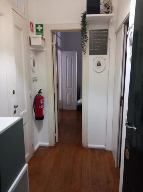 Hallway entrance of Lisbon apartment with fire extinguisher, hardwood floors, white walls, and multiple doors leading to