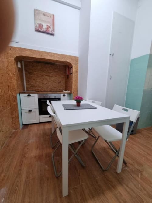 Modern dining area in Lisbon apartment with white table, chairs, and compact kitchenette with cork accent wall
