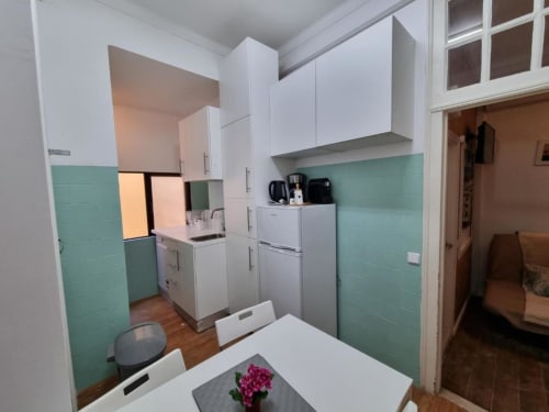 Modern kitchen in Lisbon apartment with white cabinets, mint green tiles, stainless appliances, and dining area
