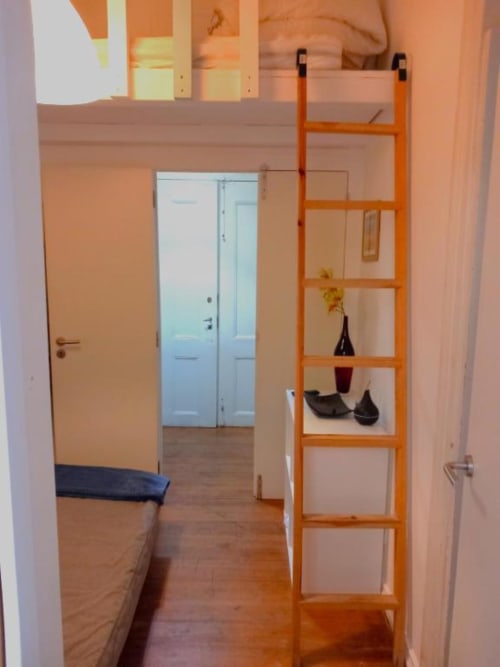Orange wooden ladder shelf with decorative items in Lisbon BnB apartment hallway with hardwood floors