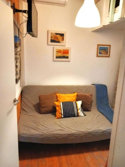 Cozy bedroom nook in Lisbon apartment with gray sofa bed, orange pillows, pendant light, and framed artwork on cream walls