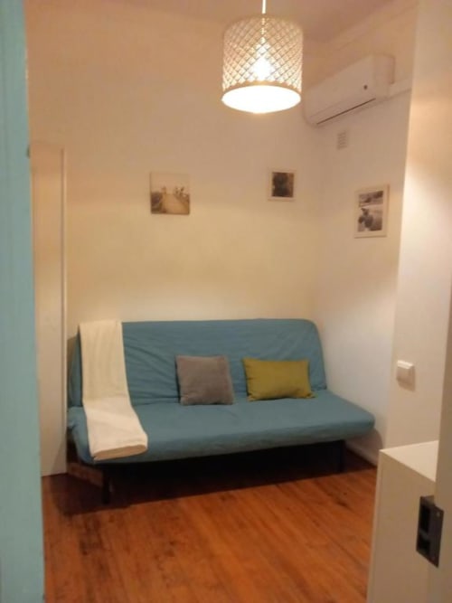 Modern living room with blue sofa bed, yellow and gray pillows, wooden floors, pendant lamp, and framed artwork in Lisbon