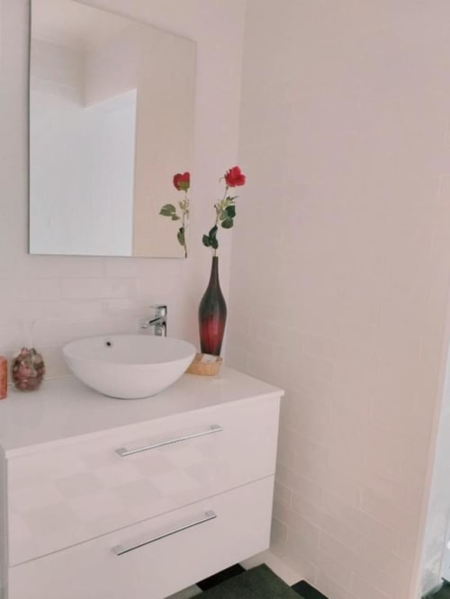 Modern white bathroom sink with red roses in vase at Charm Discovery Experiences Lisbon apartment