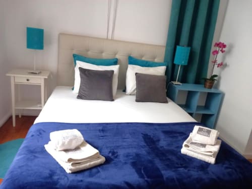 Modern bedroom in Lisbon apartment with blue velvet duvet, teal headboard, gray pillows, and fresh white towels on bed