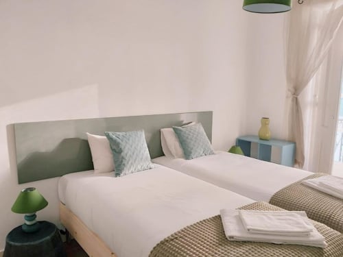 Bright modern bedroom in Lisbon B&B with twin beds, sage green headboard, white linens, and green accent lighting