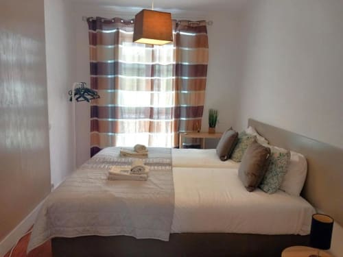 Bright bedroom in Lisbon BnB with two beds, striped curtains, pendant lamp, and modern minimalist decor