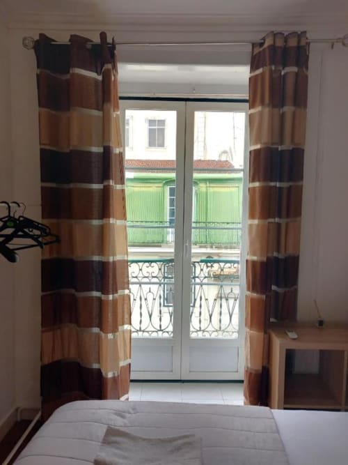 Bedroom with striped curtains and glass doors opening to Lisbon balcony view at Charm Discovery Experiences