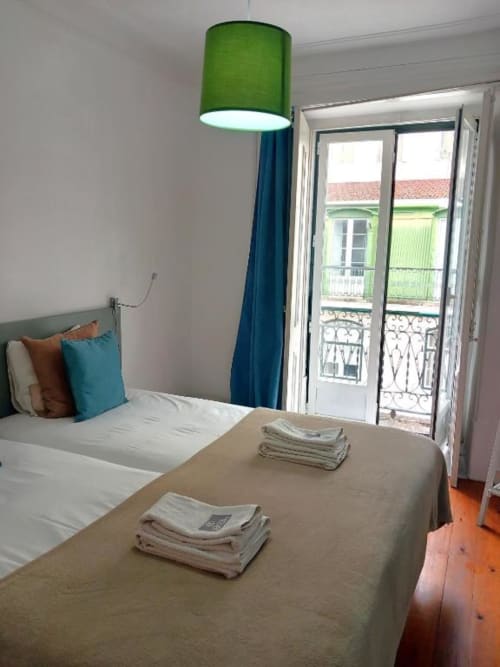 Bright bedroom in Lisbon B&B with twin beds, green pendant lamp, French doors to balcony, hardwood floors