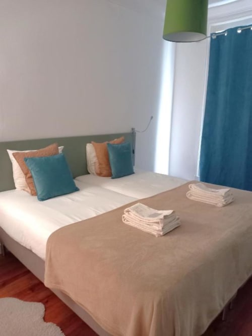 Modern bedroom at Charm Discovery Experiences in Lisbon with green headboard, teal and orange pillows, white linens, and
