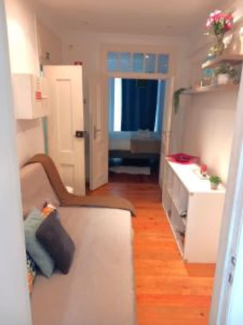 Lisbon apartment entryway with orange hardwood floors, white walls, open-plan living area, blue-framed window, and potted