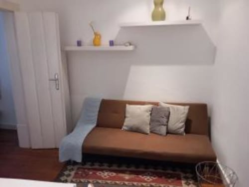 Cozy living room in Lisbon apartment with brown sofa bed, decorative pillows, white walls, floating shelf, and hardwood
