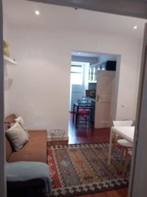 Open-plan Lisbon apartment interior with living area, dining table, kitchen doorway, and hardwood floors