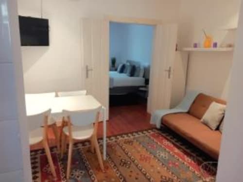 Lisbon apartment living room with dining table, orange sofa, TV, and bedroom view at Charm Discovery Experiences