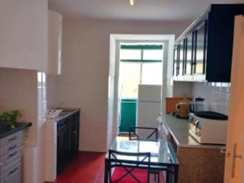 Modern kitchen in Lisbon apartment with red floor, white cabinets, stove, and dining area with green balcony view