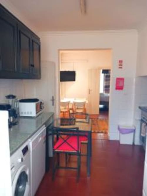 Modern kitchen and dining area in Lisbon apartment with red chairs, white appliances, and wooden floors opening to living