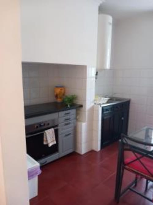 Compact kitchen in Lisbon apartment with stove, oven, white cabinetry, and red tile flooring
