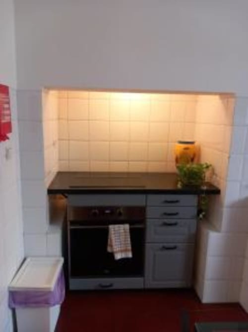 Compact kitchen in Lisbon apartment with black cabinets, oven, stovetop, and beige tile backsplash